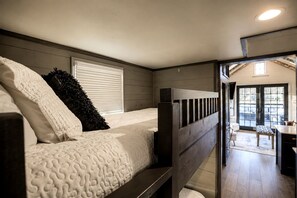 A bedroom with a bunk bed, a window with blinds, and a view of a dining area.