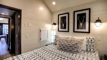 A bedroom with a bed, two framed pictures, a wall-mounted light, and a door leading to another room.