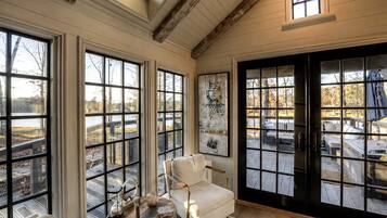 A room with large windows, a white armchair, a round table, and a view of a deck with outdoor furniture.