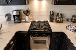 Una cocina con estufa a gas, cafetera y diferentes utensilios de cocina.