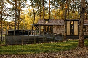 Une cabane moderne avec une façade en pierre, une terrasse en bois et une porte en verre.