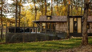 A modern cabin with a stone exterior, a wooden deck, and a glass door.