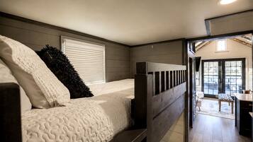 A bedroom with a bunk bed, a window with blinds, and a view of a dining area.