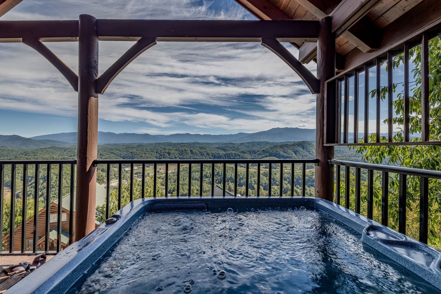 A hot tub with a wooden deck and metal railing, overlooking a mountainous landscape.