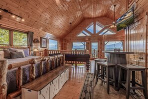 L’intérieur d’une cabane est doté d’un plafond en bois, d’un lit offrant une vue imprenable, d’un coin repas et d’une grande fenêtre donnant sur un paysage montagneux.