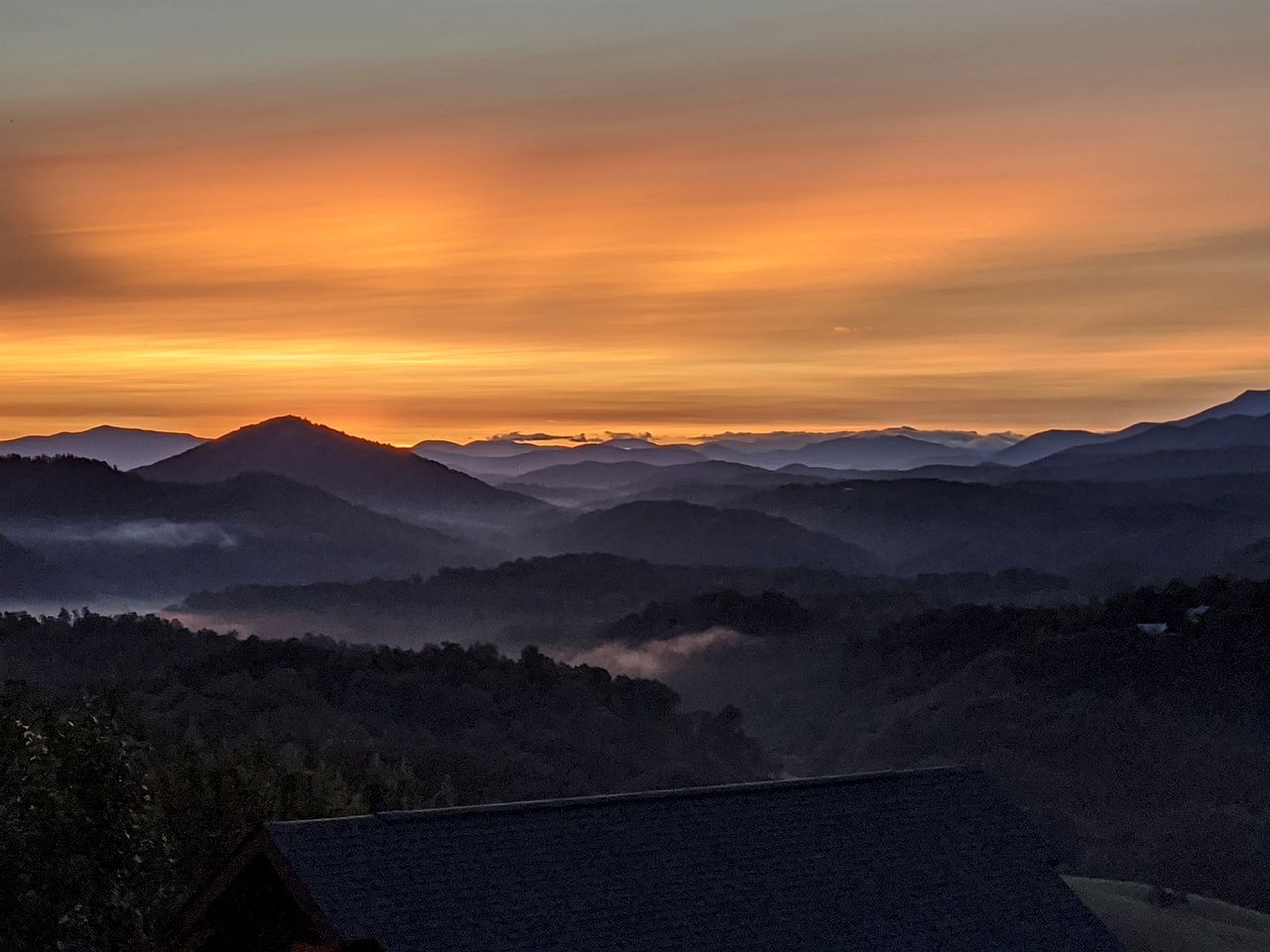 A mountainous landscape with a house in the foreground.