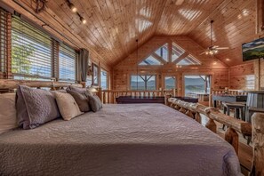 L’intérieur d’un chalet en bois, avec un grand lit, un coin repas et une vue par les fenêtres.