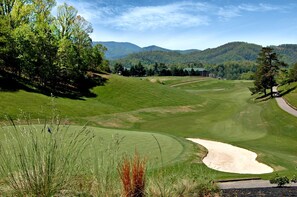 A golf course with a sand bunker, trees, and a mountain backdrop. - Modern Mountain Cabin Retreat with Game Room and Outdoor Pool in Sevierville, Tennessee (Sevierville)