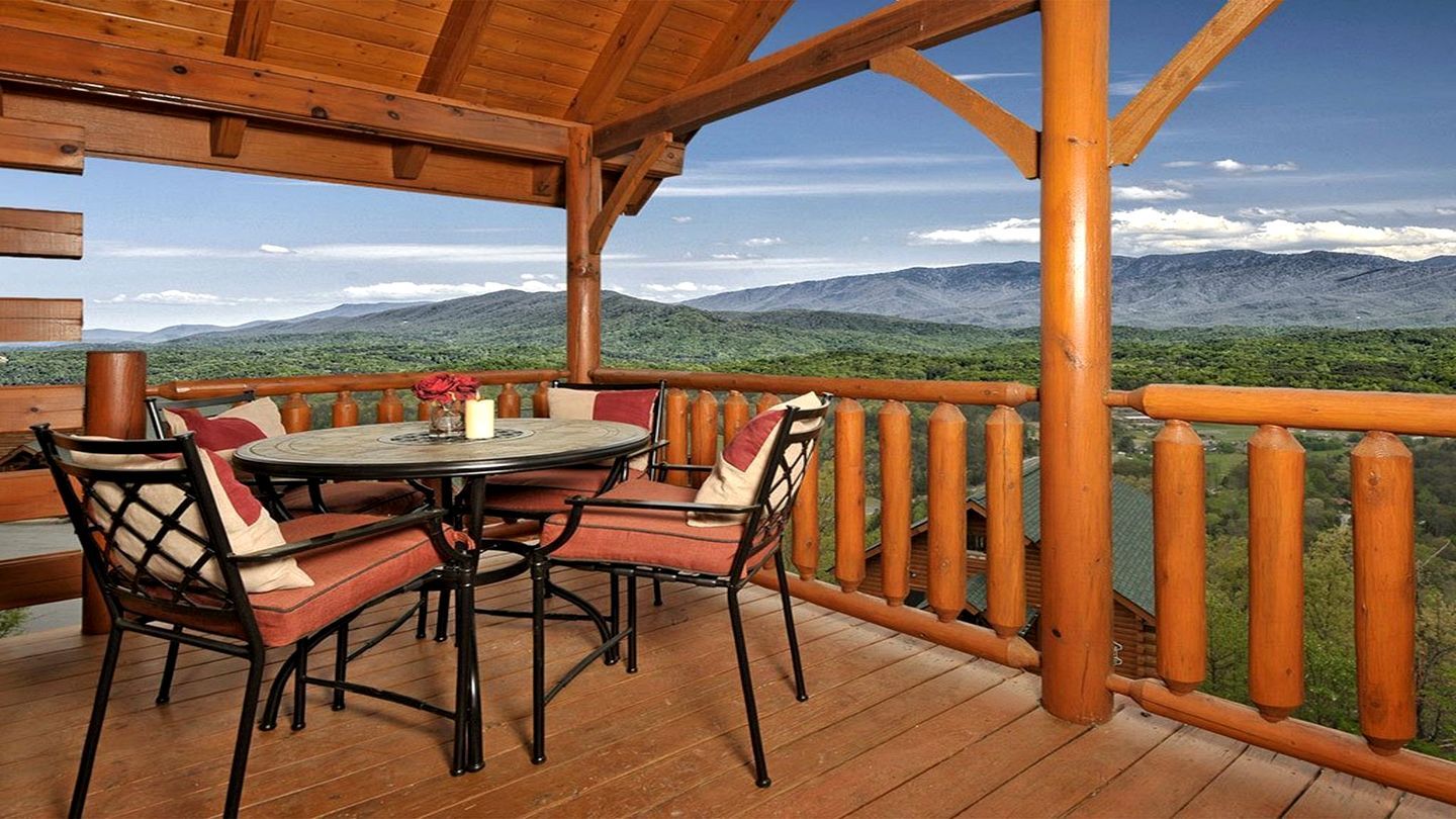 A wooden deck with a round table and chairs, overlooking a mountainous landscape.
