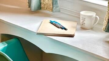 A room with a teal chair, a white desk, a notebook, a pen, and a mug.