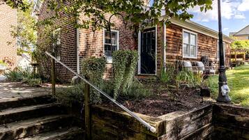 A brick house with a wooden front porch, steps leading to the entrance, and a garden area with plants and a wooden planter.