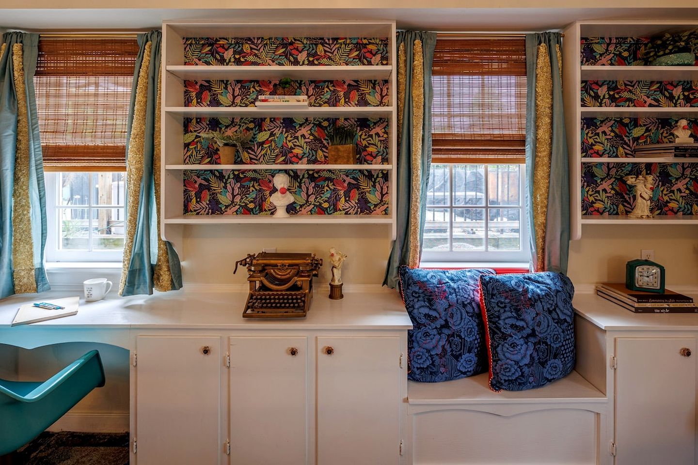 Una habitación con un asiento junto a la ventana, estanterías con papel tapiz estampado, una máquina de escribir y un reloj.