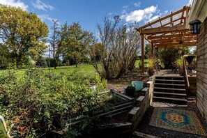 Un jardin agrémenté d’une pergola en bois, d’un escalier menant à un espace abrité et d’un tapis à motifs.