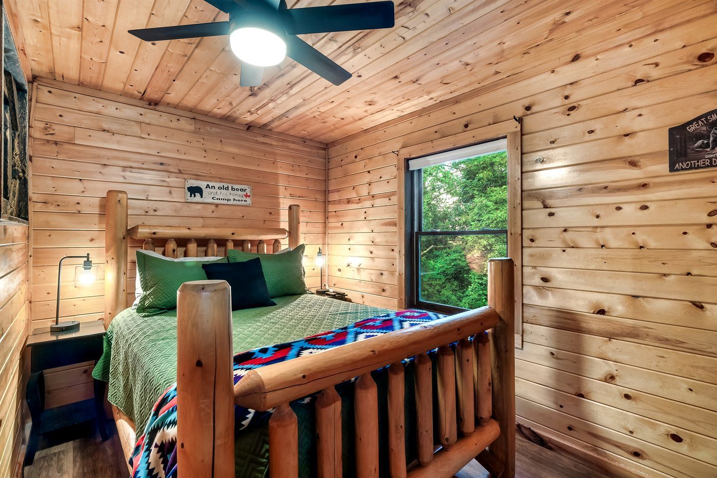 A wooden cabin bedroom with a bed, a headboard, a window, and a ceiling fan.