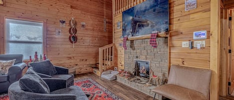 A cozy cabin interior with a fireplace, wooden walls, and a ceiling fan.