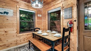 A wooden cabin interior with a dining table set for four, two windows, a fire extinguisher, and a sign about cabin rules. - Extraordinary Retreat with Hot-Tub and Indoor Pool in Tennessee (Sevierville)