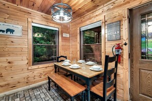 A wooden cabin interior with a dining table set for four, two windows, a fire extinguisher, and a sign about cabin rules. - Extraordinary Retreat with Hot-Tub and Indoor Pool in Tennessee (Sevierville)