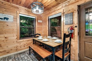 Ein Holzblockhaus-Innenraum mit einem Esstisch, gedeckt für vier Personen, zwei Fenstern, einem Feuerlöscher und einem Schild mit Regeln für das Blockhaus.