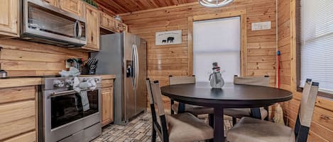 A wooden cabin interior with a kitchen, dining table, and chairs.