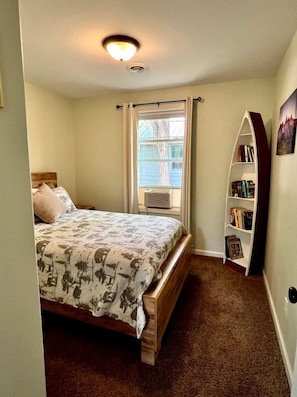 A bedroom with a bed, a window with curtains, a bookshelf, and a ceiling light. - Sweet Cabin with Furnished Patio Suitable for Six in South Dakota (Hot Springs)