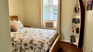 A bedroom with a bed, a window with curtains, a bookshelf, and a ceiling light. - Sweet Cabin with Furnished Patio Suitable for Six in South Dakota (Hot Springs)