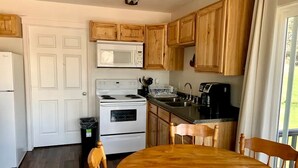 A kitchen with wooden cabinets, a white stove, a microwave, and a dining table with chairs. - Sweet Cabin with Furnished Patio Suitable for Six in South Dakota (Hot Springs)