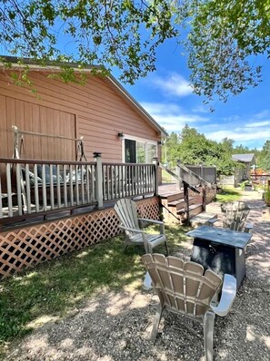 A wooden deck with Adirondack chairs, a small table, and a covered patio area.