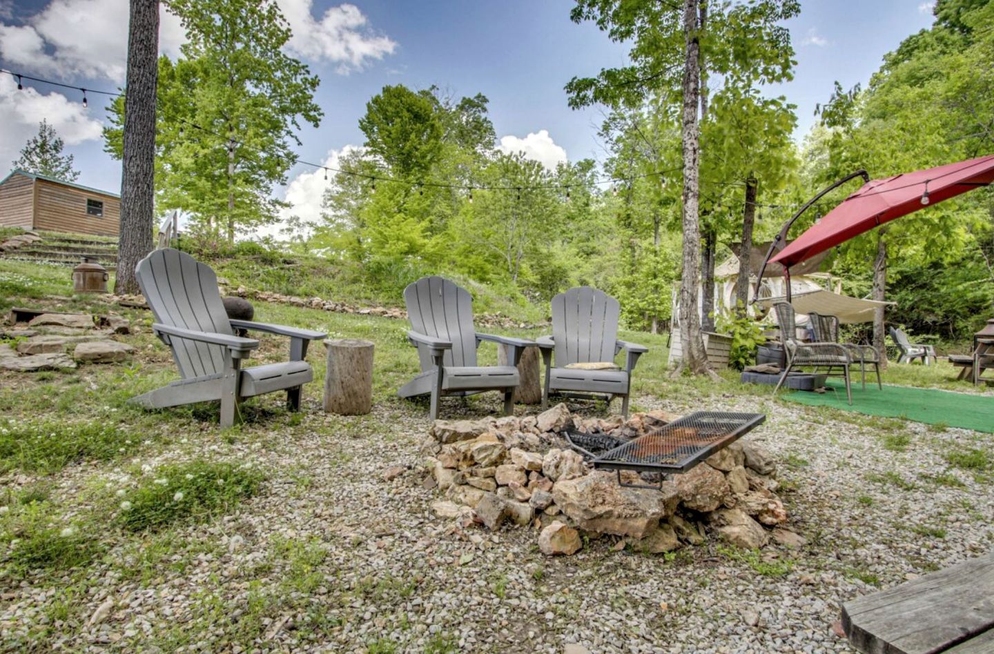 A campsite with Adirondack chairs, a fire pit, and a covered area.