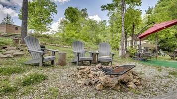 A campsite with Adirondack chairs, a fire pit, and a covered area.