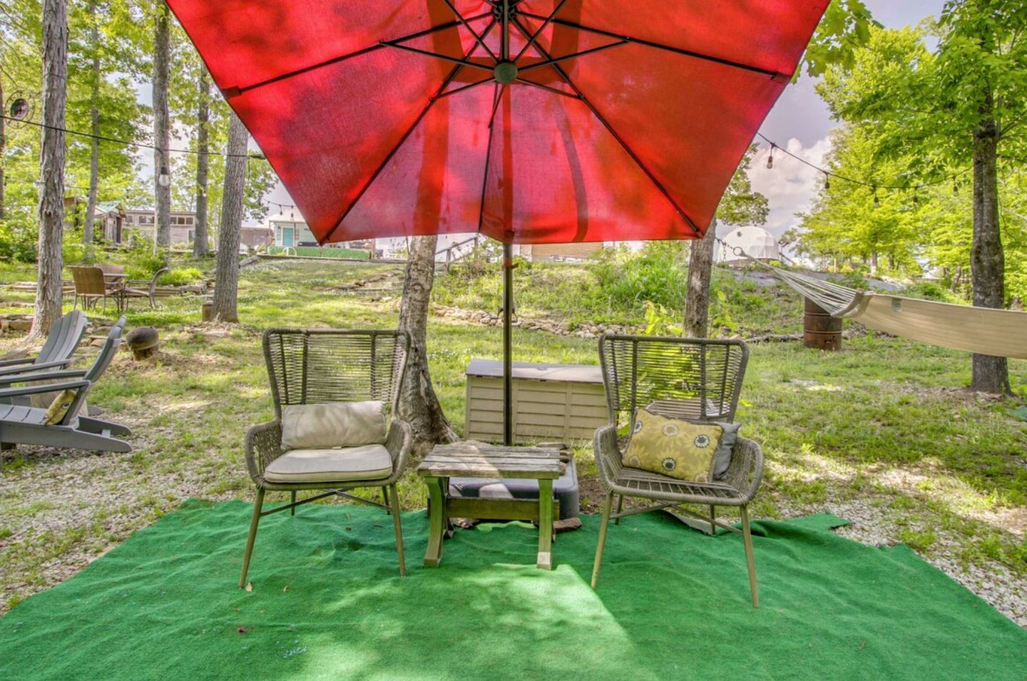 A patio area with outdoor furniture, including two wicker chairs and a table, under a red umbrella.