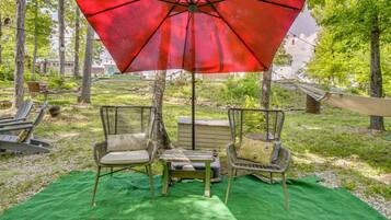 A patio area with outdoor furniture, including two wicker chairs and a table, under a red umbrella.