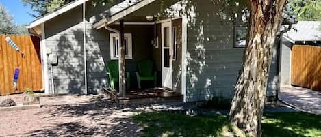 A single-story house with a covered porch, a small front yard, and a tree.
