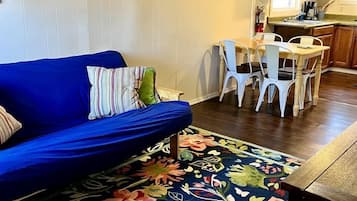 A living room with a blue sofa, a floral rug, and a dining area with white chairs.