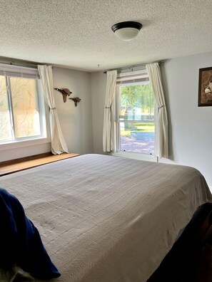 Ein Schlafzimmer mit einem großen Bett, zwei mit Vorhängen versehenen Fenstern, einer Deckenleuchte und einer an der Wand befestigten Vogeldekoration.