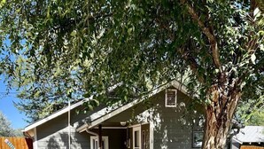 A single-story house with a covered porch, a small front yard, and a tree.