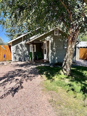 A single-story house with a covered porch, a small front yard, and a tree.