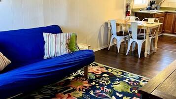 A living room with a blue sofa, a floral rug, and a dining area with white chairs.