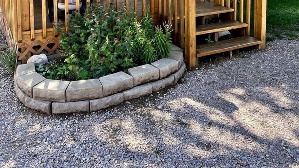 A cabin with a wooden deck, a stone planter with greenery, and a large tree.