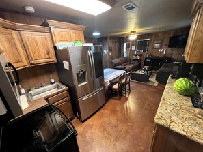 A kitchen with wooden cabinets, a stainless steel refrigerator, a dining table with chairs, and a countertop with a watermelon. - Family Style Glamping in Pet-Friendly Rental at Lake Godstone, Texas (Graford)