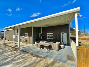 A covered outdoor seating area with a table and chairs, a grill, and a window with a view. - Family Style Glamping in Pet-Friendly Rental at Lake Godstone, Texas (Graford)