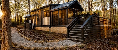 A cabin with a wooden exterior, a stone foundation, and a staircase leading to the entrance.