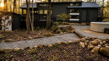 Una cabaña moderna con un camino de grava, rodeada de árboles y un jardín de rocas.