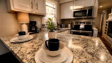 Una cocina con encimeras de granito, armarios blancos, electrodomésticos de acero inoxidable y una planta en maceta.
