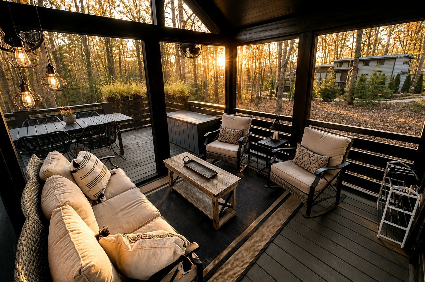 Une terrasse extérieure aménagée avec un canapé, des fauteuils et une table, entourée d’une rambarde en bois et donnant sur une zone boisée.