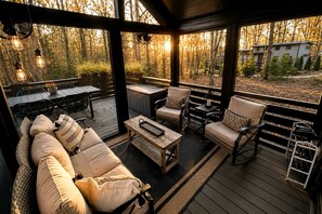 An outdoor deck with a sofa, chairs, and a table, surrounded by a wooden railing and overlooking a forested area. - Chic Tiny Cabin with Jacuzzi, Screened Porch and Grill in Tennessee (Tracy City)