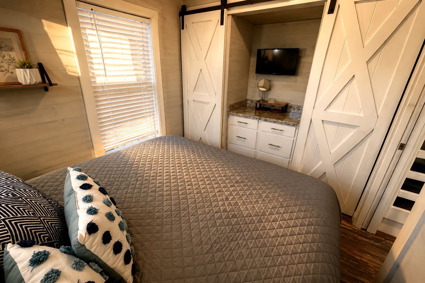 Ein Schlafzimmer mit einem Bett, einem Schminktisch, einem Fernseher und einem Fenster mit Jalousien.