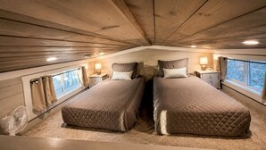 A cozy bedroom with two beds, a fan, and a window with curtains. - Chic Tiny Cabin with Jacuzzi, Screened Porch and Grill in Tennessee (Tracy City)