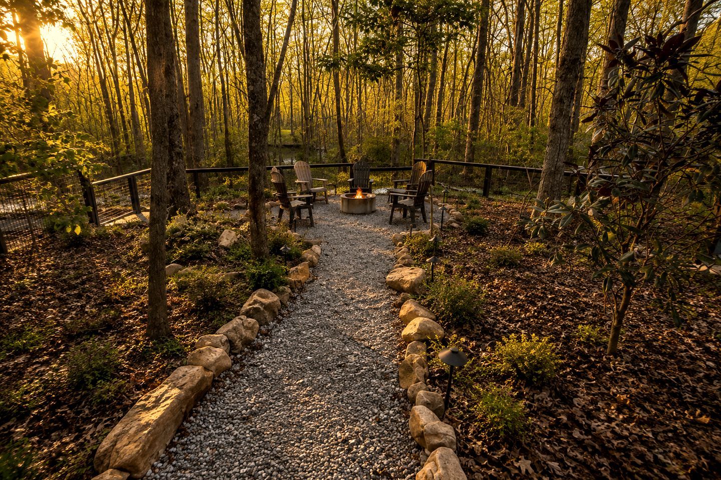Un área boscosa con un sendero de grava que conduce a un espacio de descanso con sillas y una chimenea.