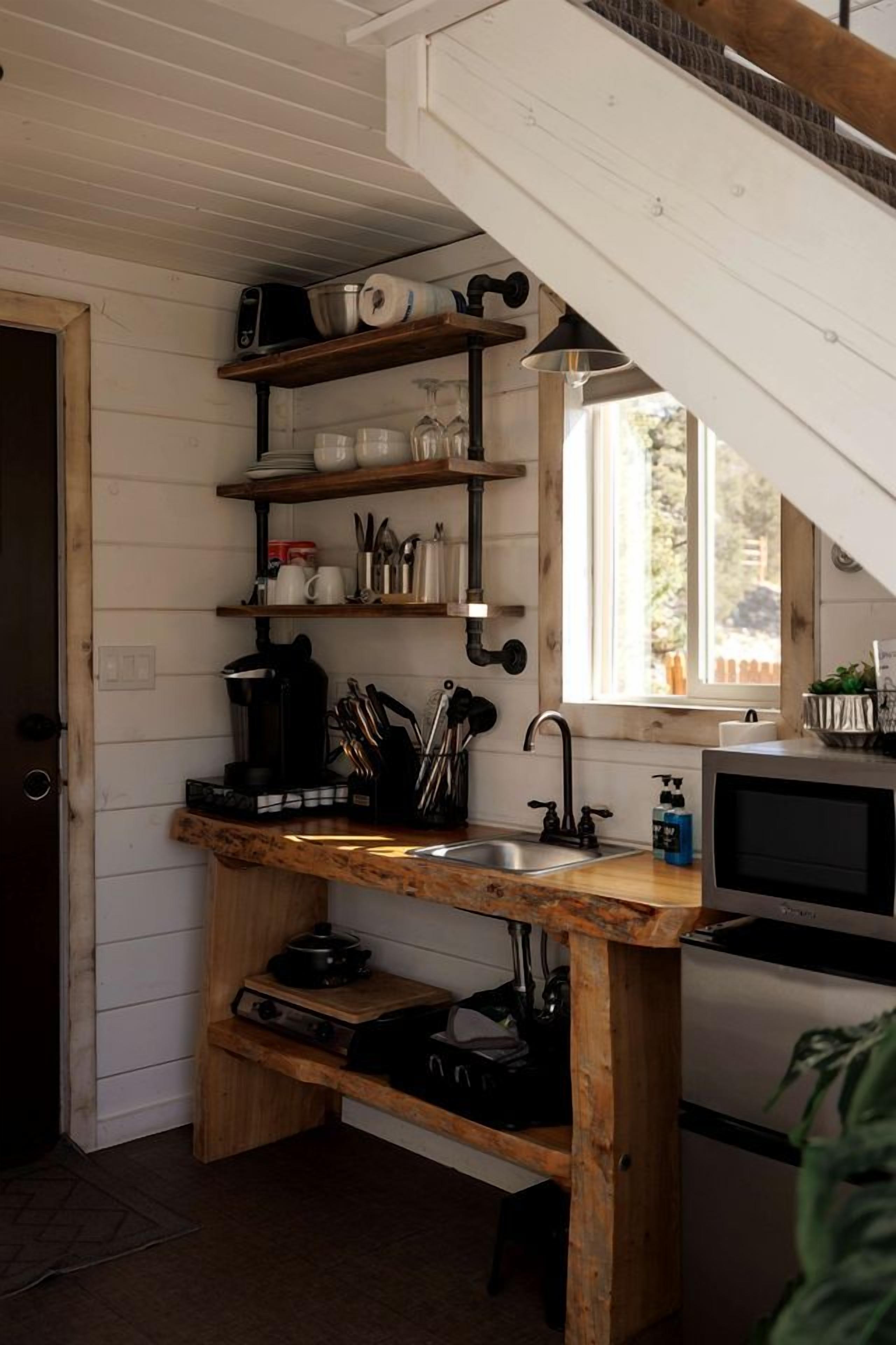 A compact kitchen with wooden shelves, a sink, and a microwave.