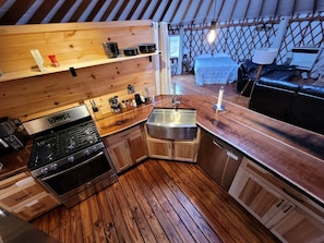Cocina compacta con suelo de madera, estufa, lavamanos y comedor con mesa y sillas.